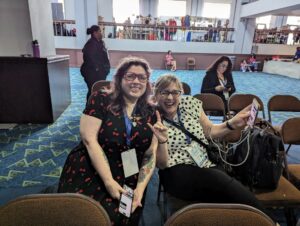 Two people sitting at a conference and smiling at the camera